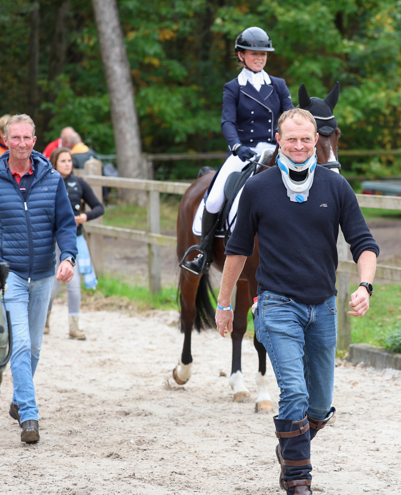 Nina Hut op weg naar de dressuurring met voor haar de na een bedrijfsongeval met een nekbrace lopende partner Tarik van Boggelen en links haar dressuurcoach Frank Hosmar.